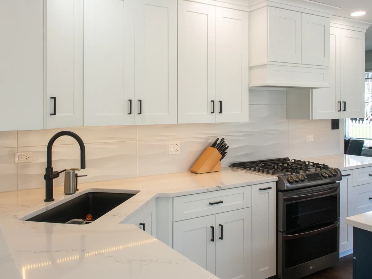 Modern kitchen with white cabinets, marble countertop, stainless steel appliances and white decor.