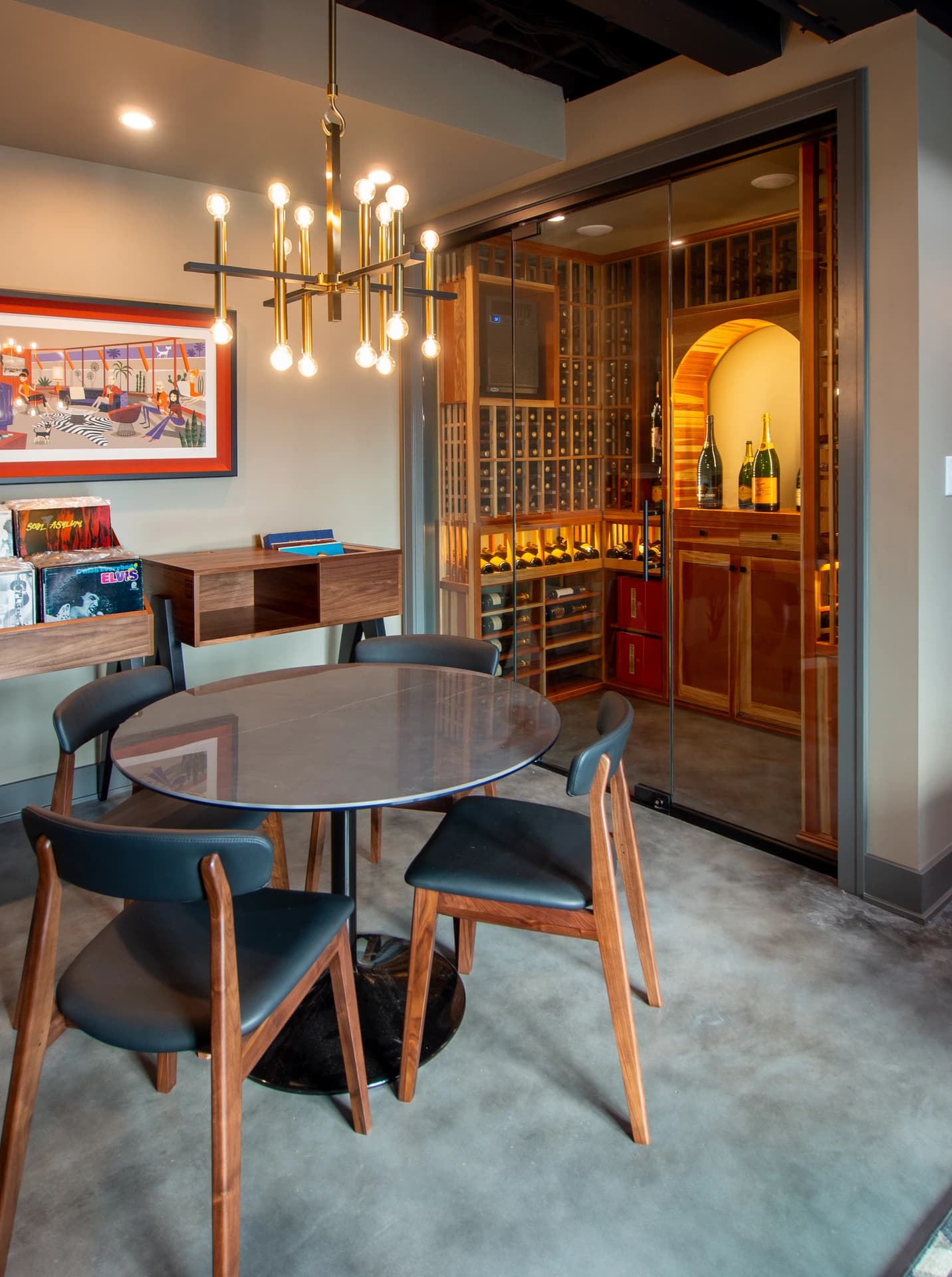 Modern wine cellar with wooden table, black chairs, red and white wall, and glass doors.